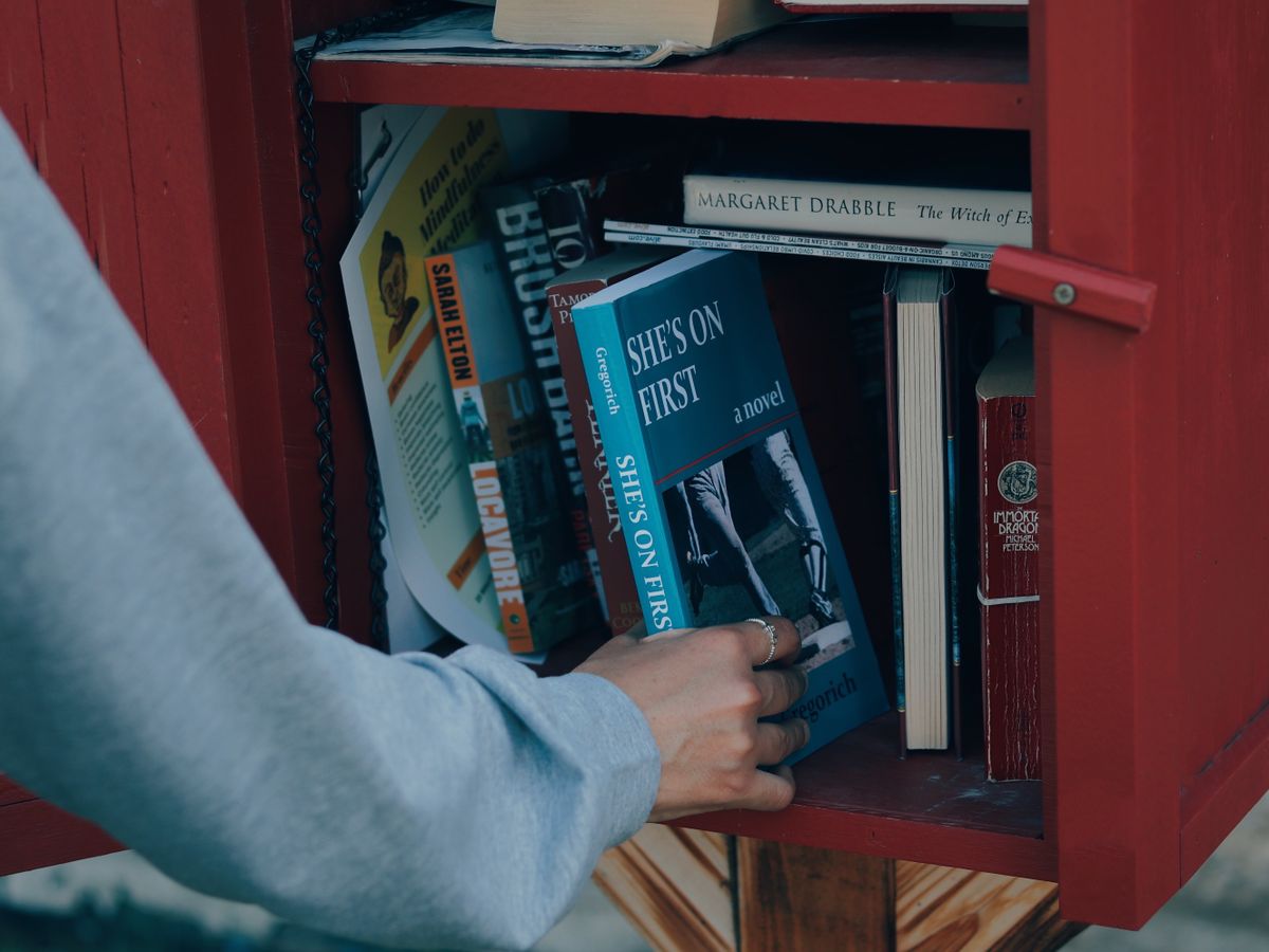A hand selecting a book from a community book-sharing cabinet